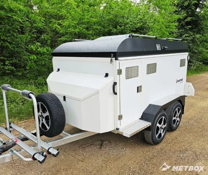 White METBOX dog trailer with spare tire and hitch-mounted bike rack on a forest road